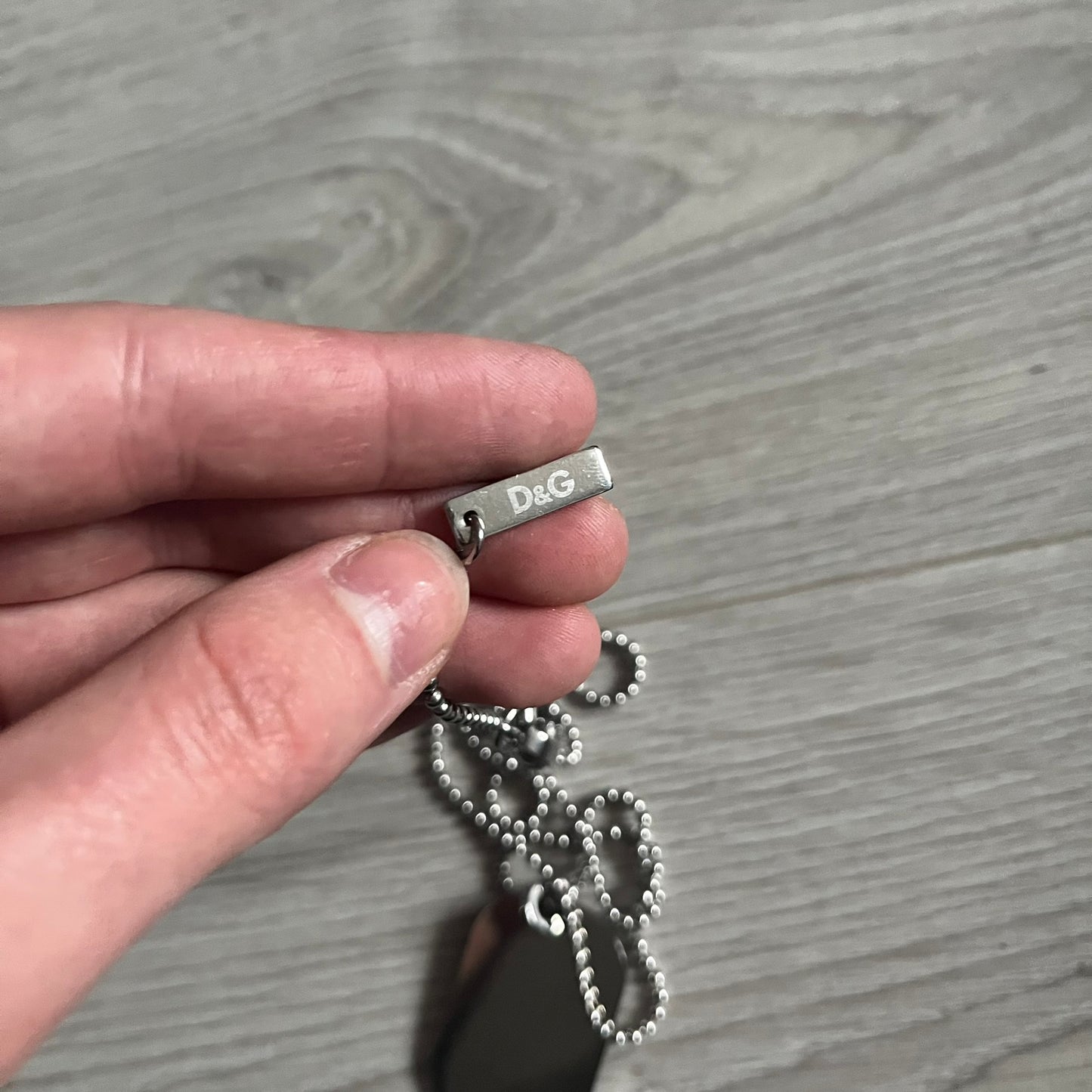 Dolce &amp; Gabbana Cowboy Dog Tag Necklace, model DJ0633. Features a silver-tone metal ball chain and a dog tag with black cowboy-style D&amp;G logo and small “Dolce &amp; Gabbana” text underneath. The front of the tag is patterned with subtle white dots for added detail.