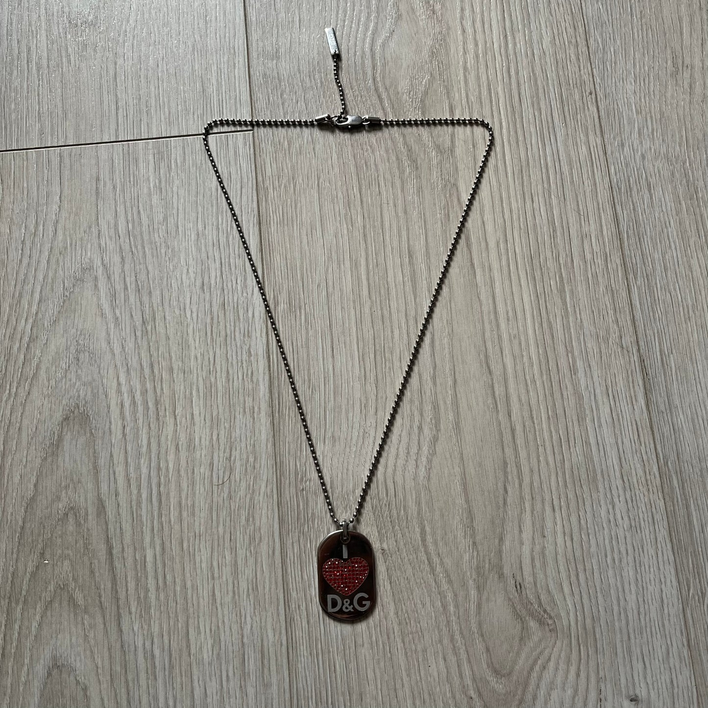 Dolce &amp; Gabbana "I ❤️ D&amp;G" Dog Tag Necklace with a silver stainless steel ball chain, featuring a dog tag engraved with a white "I," a red crystal heart, and "D&amp;G" text below, forming the "I ❤️ D&amp;G" design. A playful and collectible vintage piece.