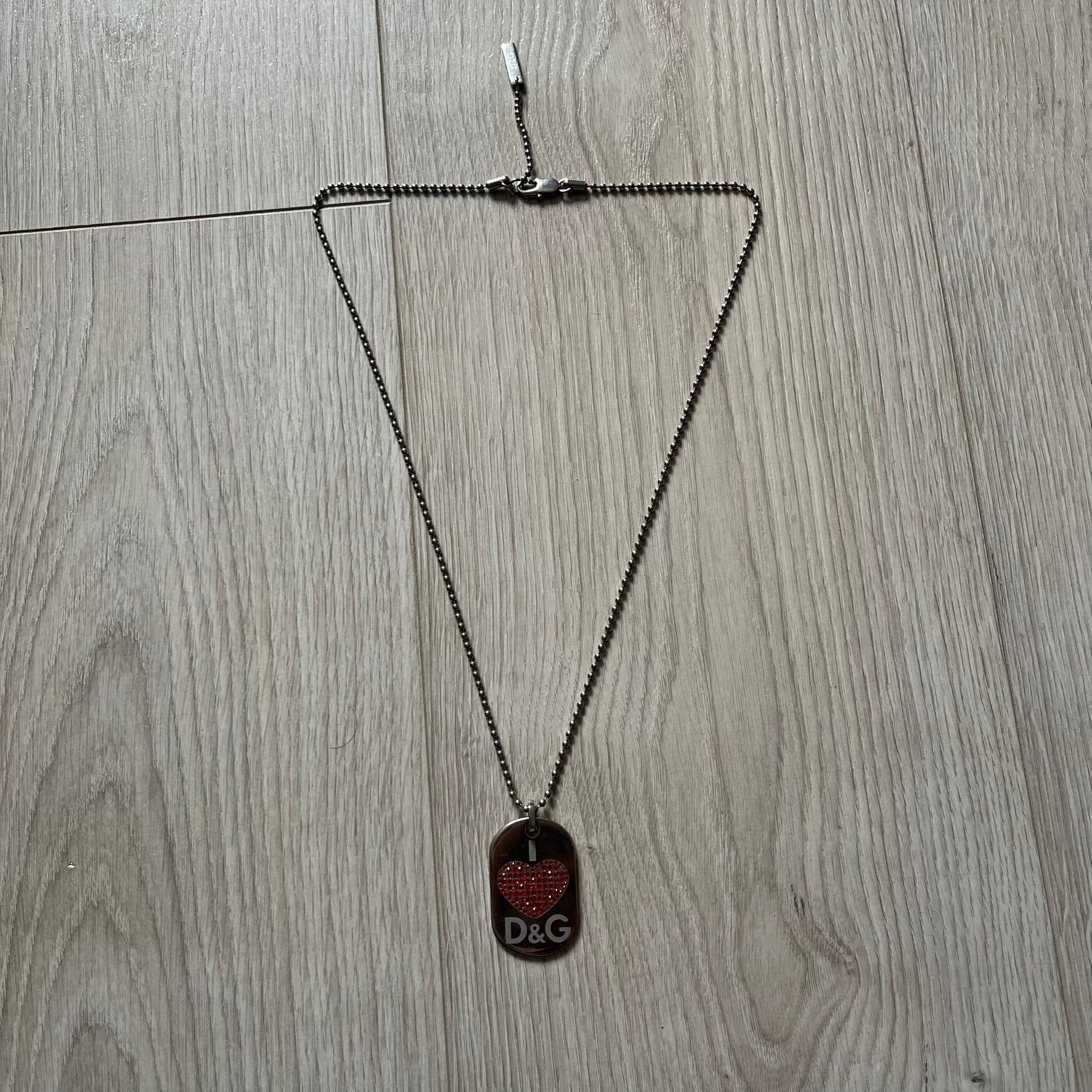 Dolce &amp; Gabbana "I ❤️ D&amp;G" Dog Tag Necklace with a silver stainless steel ball chain, featuring a dog tag engraved with a white "I," a red crystal heart, and "D&amp;G" text below, forming the "I ❤️ D&amp;G" design. A playful and collectible vintage piece.