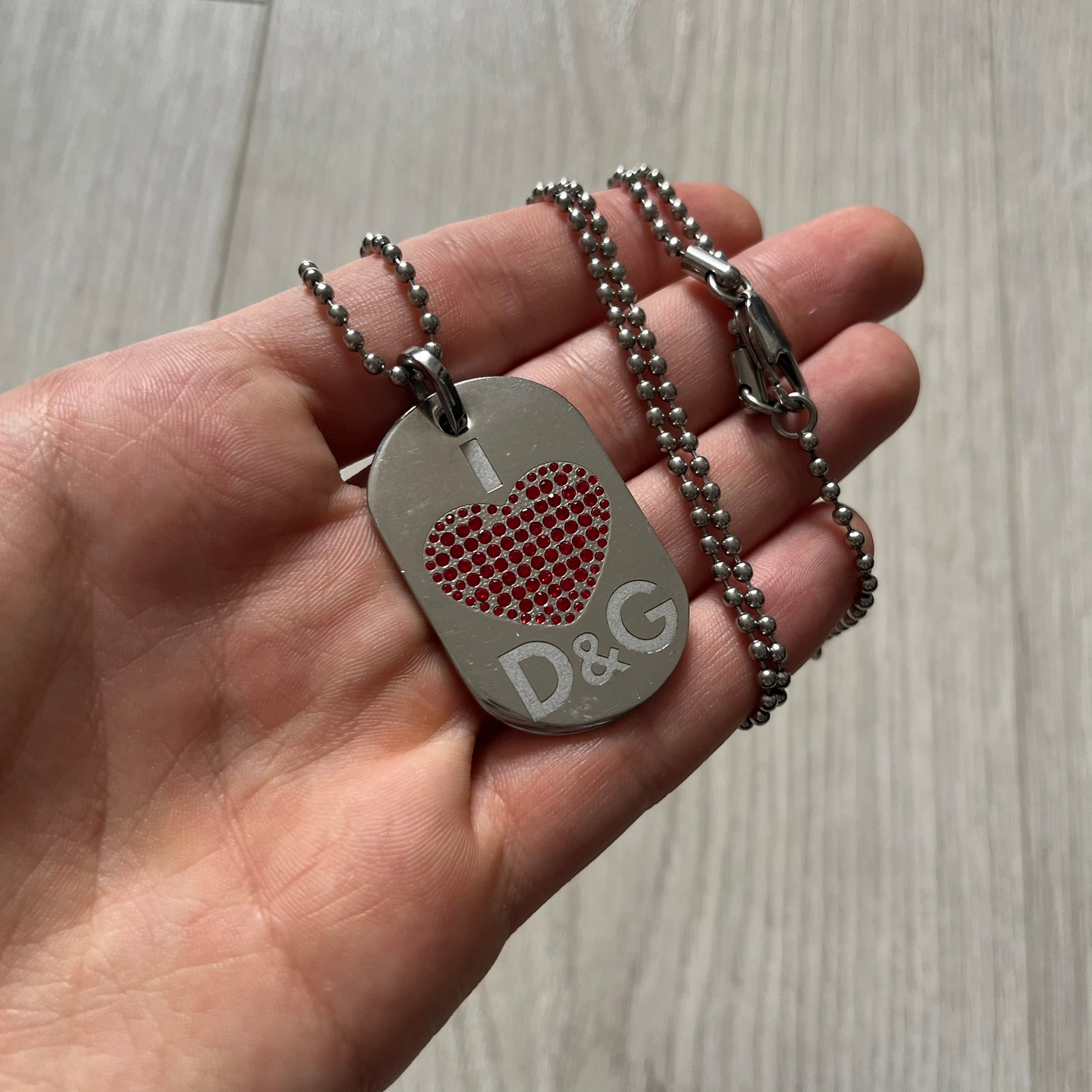 Dolce &amp; Gabbana "I ❤️ D&amp;G" Dog Tag Necklace with a silver stainless steel ball chain, featuring a dog tag engraved with a white "I," a red crystal heart, and "D&amp;G" text below, forming the "I ❤️ D&amp;G" design. A playful and collectible vintage piece.