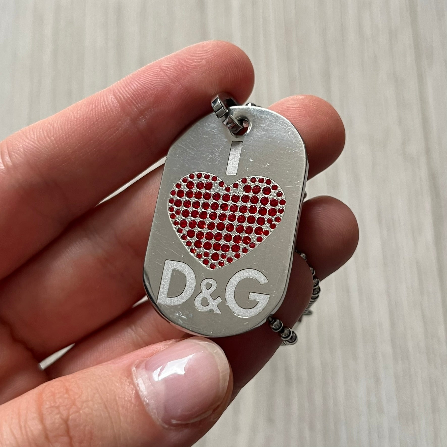 Dolce &amp; Gabbana "I ❤️ D&amp;G" Dog Tag Necklace with a silver stainless steel ball chain, featuring a dog tag engraved with a white "I," a red crystal heart, and "D&amp;G" text below, forming the "I ❤️ D&amp;G" design. A playful and collectible vintage piece.