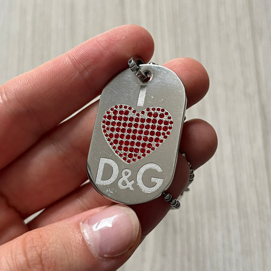Dolce &amp; Gabbana "I ❤️ D&amp;G" Dog Tag Necklace with a silver stainless steel ball chain, featuring a dog tag engraved with a white "I," a red crystal heart, and "D&amp;G" text below, forming the "I ❤️ D&amp;G" design. A playful and collectible vintage piece.