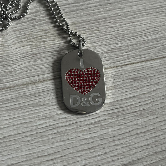 Dolce &amp; Gabbana "I ❤️ D&amp;G" Dog Tag Necklace with a silver stainless steel ball chain, featuring a dog tag engraved with a white "I," a red crystal heart, and "D&amp;G" text below, forming the "I ❤️ D&amp;G" design. A playful and collectible vintage piece. Comes with a dustbag.