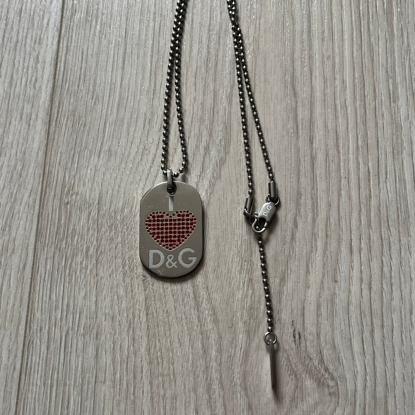 Dolce &amp; Gabbana "I ❤️ D&amp;G" Dog Tag Necklace with a silver stainless steel ball chain, featuring a dog tag engraved with a white "I," a red crystal heart, and "D&amp;G" text below, forming the "I ❤️ D&amp;G" design. A playful and collectible vintage piece.