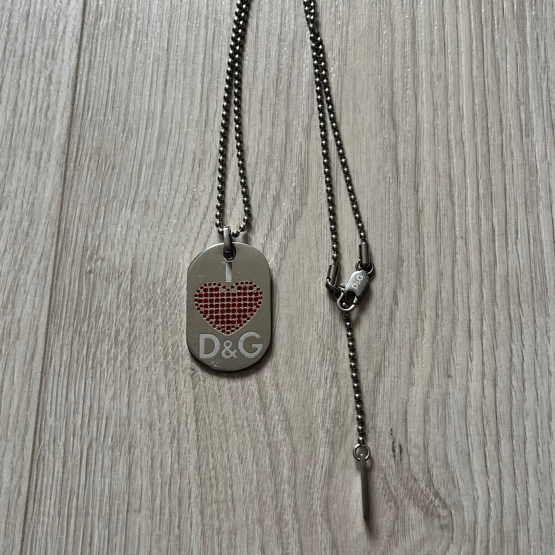 Dolce &amp; Gabbana "I ❤️ D&amp;G" Dog Tag Necklace with a silver stainless steel ball chain, featuring a dog tag engraved with a white "I," a red crystal heart, and "D&amp;G" text below, forming the "I ❤️ D&amp;G" design. A playful and collectible vintage piece.
