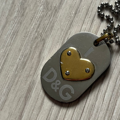 Dolce & Gabbana "I ❤️ D&G" Gold Dog Tag Necklace with a silver stainless steel ball chain, featuring a dog tag engraved with a light "I", a gold metal heart with 3 visible screws, and "D&G" text below, forming the "I ❤️ D&G" design. A playful and collectible vintage piece.