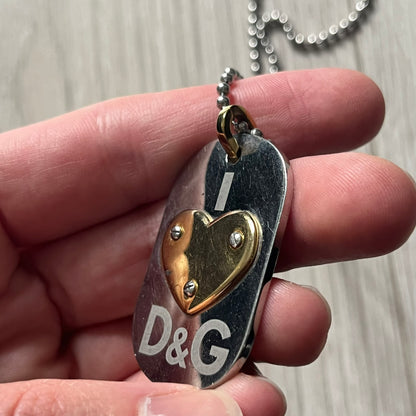 Dolce & Gabbana "I ❤️ D&G" Gold Dog Tag Necklace with a silver stainless steel ball chain, featuring a dog tag engraved with a light "I", a gold metal heart with 3 visible screws, and "D&G" text below, forming the "I ❤️ D&G" design. A playful and collectible vintage piece.