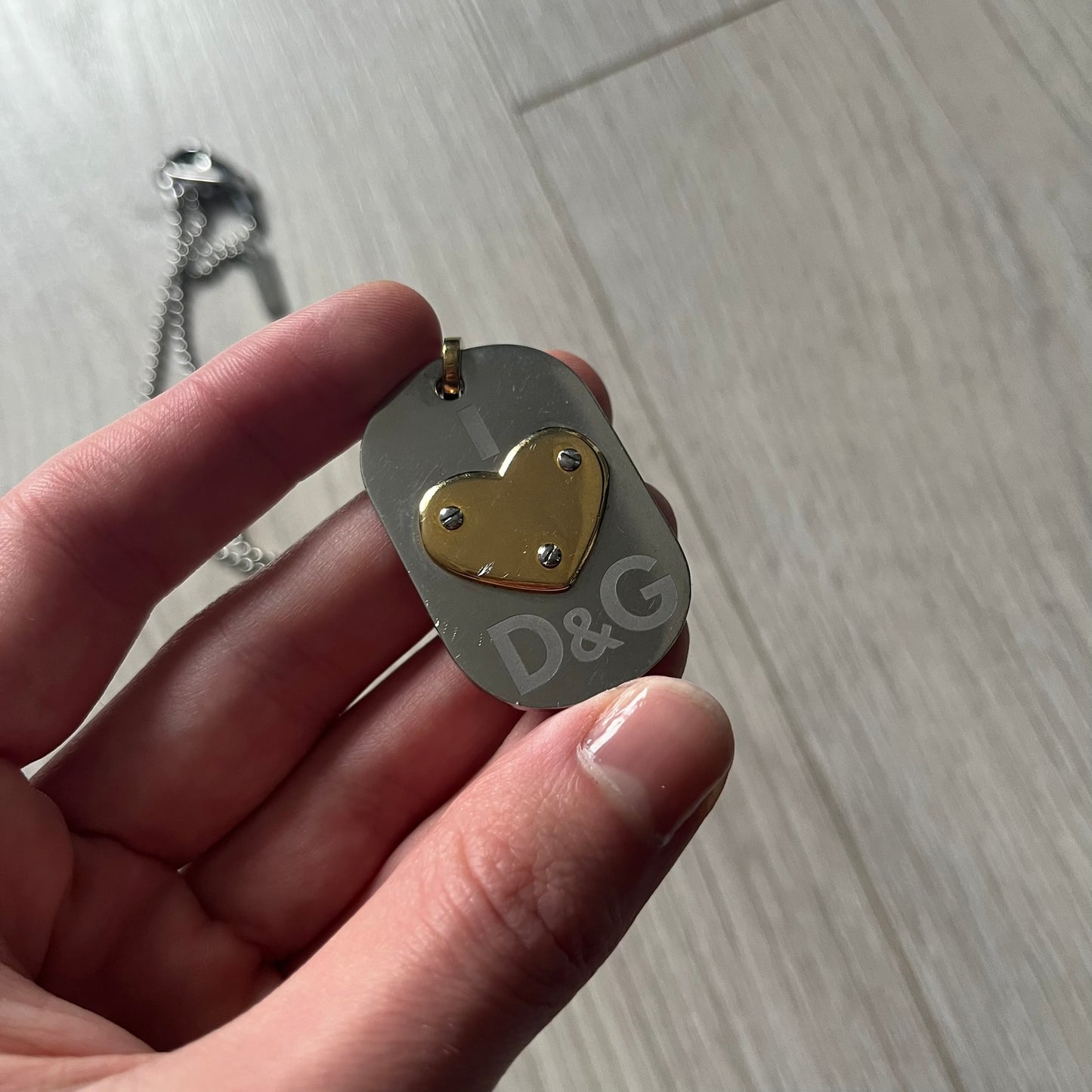 Dolce & Gabbana "I ❤️ D&G" Gold Dog Tag Necklace with a silver stainless steel ball chain, featuring a dog tag engraved with a light "I", a gold metal heart with 3 visible screws, and "D&G" text below, forming the "I ❤️ D&G" design. A playful and collectible vintage piece.