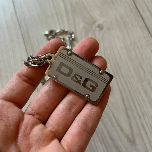Dolce &amp; Gabbana Propaganda Dog Tag Necklace, featuring a silver stainless steel square tag with four visible screws and the D&amp;G logo engraved on the front. The tag hangs from a durable cable chain, combining sturdy construction with clean, industrial-inspired detailing.
