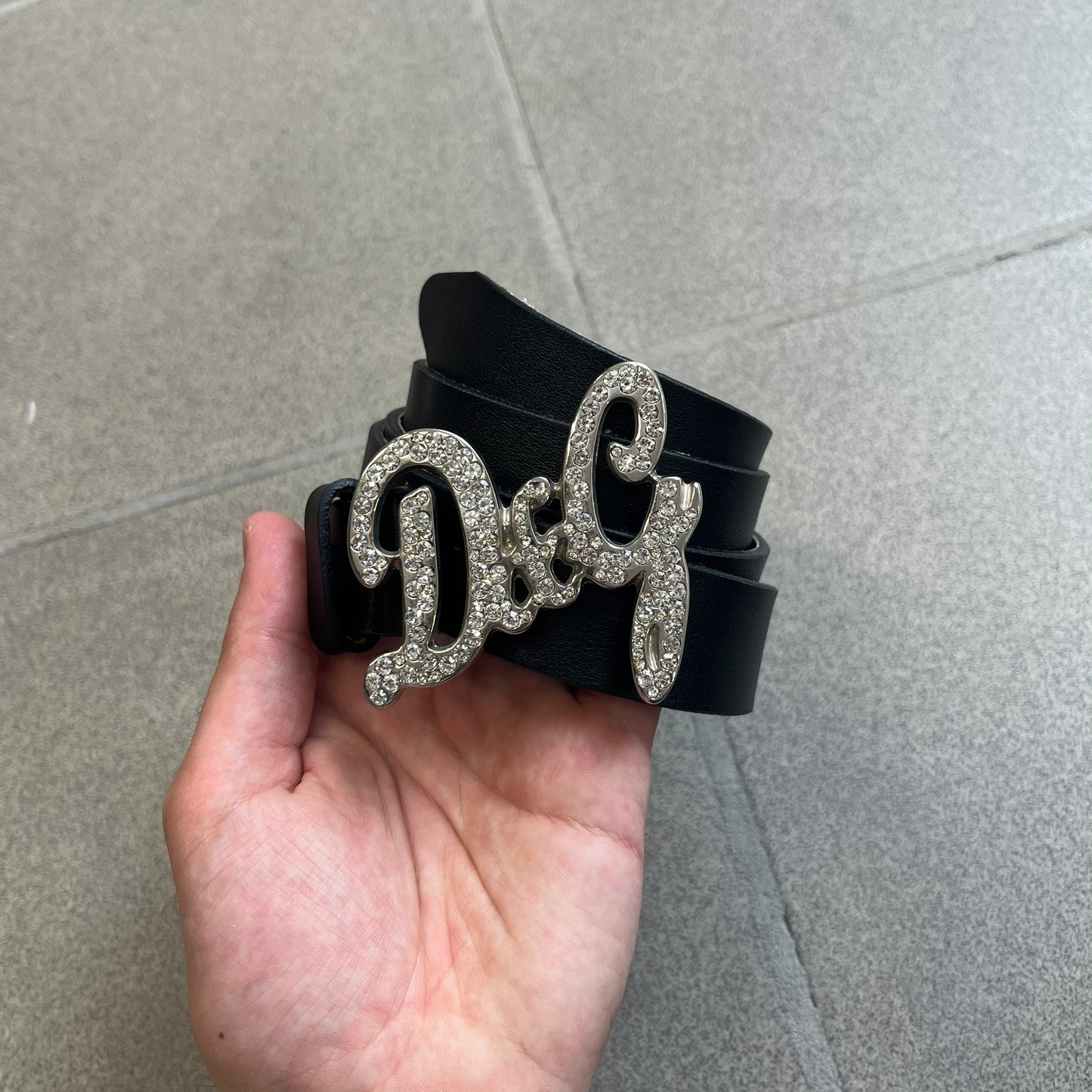 Dolce &amp; Gabbana 2000s Black Crystal Buckle Belt features a black leather strap with a stainless steel D&amp;G logo buckle. The buckle has a decorative italic-style font and is fully covered with crystal/rhinestone detailing on the front. Made in Italy.