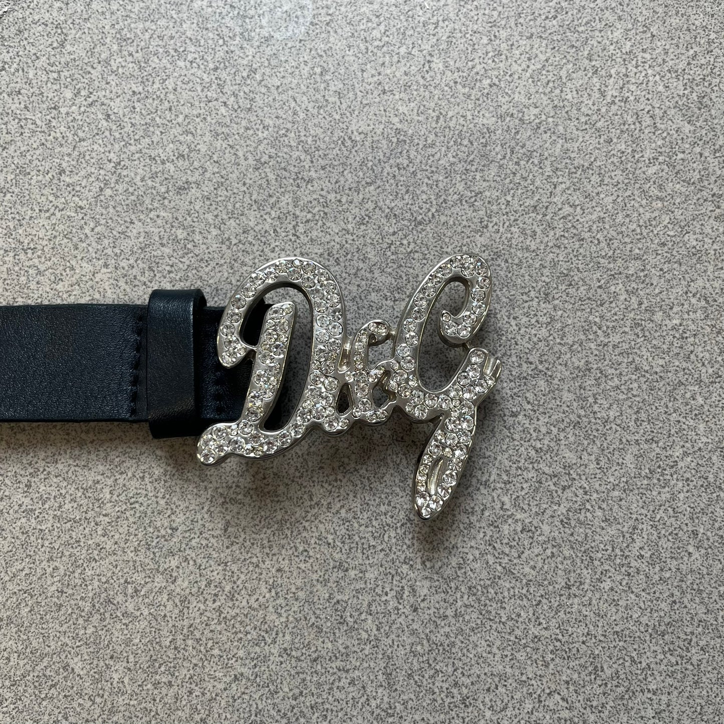 Dolce &amp; Gabbana 2000s Black Crystal Buckle Belt features a black leather strap with a stainless steel D&amp;G logo buckle. The buckle has a decorative italic-style font and is fully covered with crystal/rhinestone detailing on the front. Made in Italy.