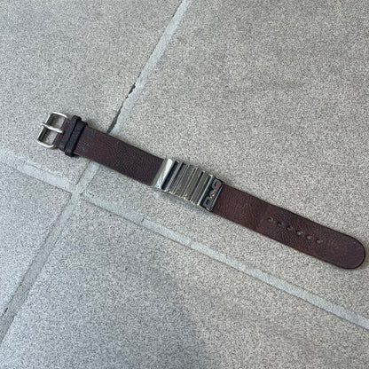 Dolce & Gabbana 2000's Brown Leather Bracelet features brown leather straps with an adjustable fit and a stainless steel central plaque. The plaque has a raised wavy texture on the front and a D&G logo underneath, while the leather straps have small D&G and “Genuine Leather” tags.
