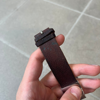 Dolce & Gabbana 2000's Brown Leather Bracelet features brown leather straps with an adjustable fit and a stainless steel central plaque. The plaque has a raised wavy texture on the front and a D&G logo underneath, while the leather straps have small D&G and “Genuine Leather” tags.
