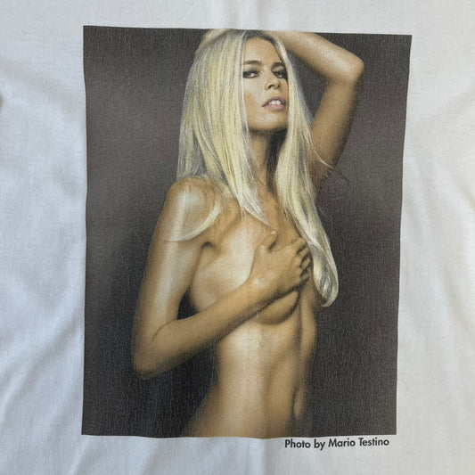 Dolce &amp; Gabbana 2000’s Claudia Schiffer Photo White Tee is a white T-shirt with a photo of naked Claudia Schiffer on the front, covering her chest with her hand, and small “Photo by Mario Testino” text below it. The upper back has “D&amp;G 18 La Lune” text. The shirt is constructed inside-out style, with the stitching visible along the sides.