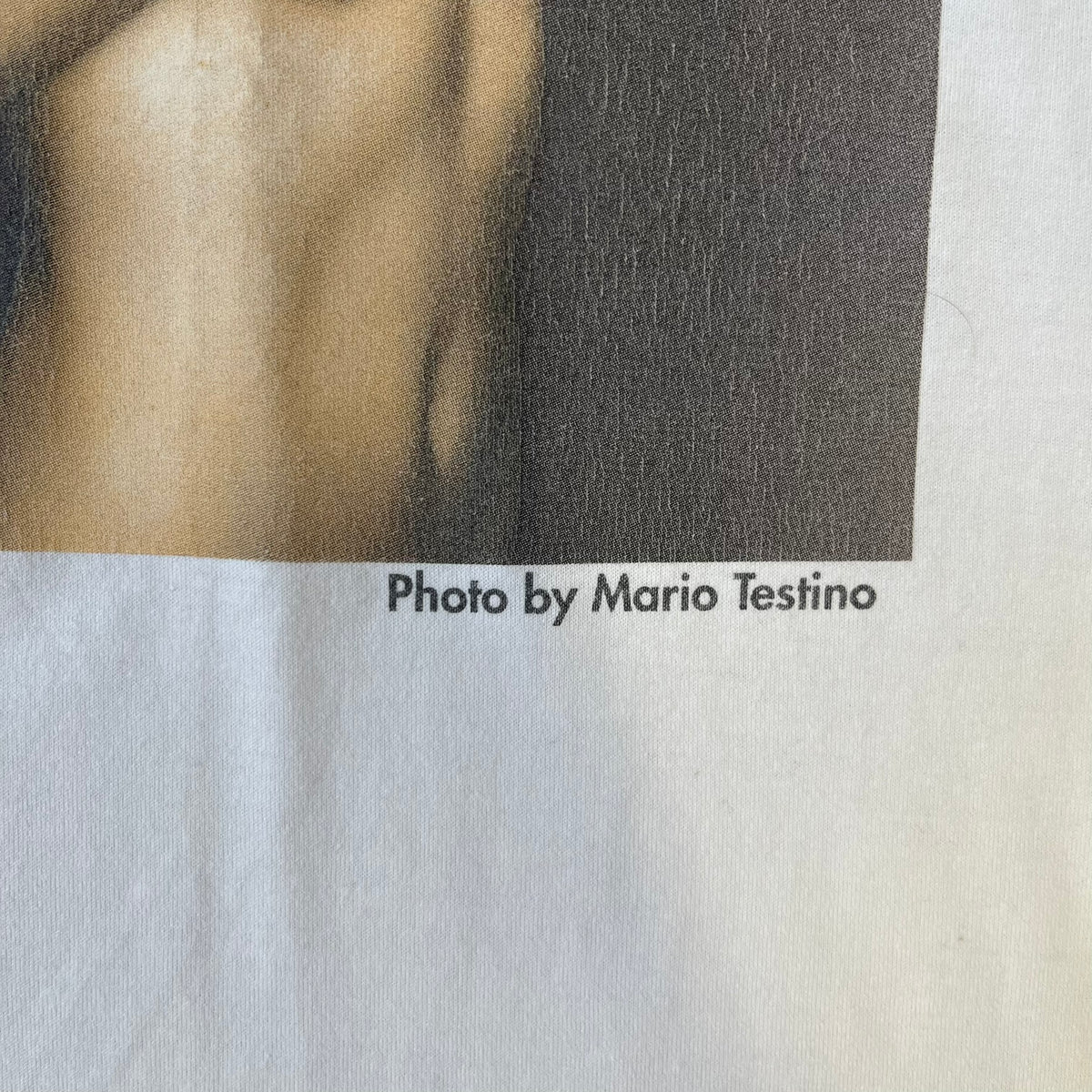 Dolce &amp; Gabbana 2000’s Claudia Schiffer Photo White Tee is a white T-shirt with a photo of naked Claudia Schiffer on the front, covering her chest with her hand, and small “Photo by Mario Testino” text below it. The upper back has “D&amp;G 18 La Lune” text. The shirt is constructed inside-out style, with the stitching visible along the sides.