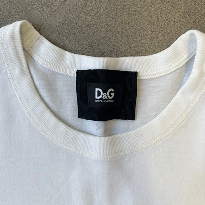 Dolce &amp; Gabbana 2000’s Claudia Schiffer Photo White Tee is a white T-shirt with a photo of naked Claudia Schiffer on the front, covering her chest with her hand, and small “Photo by Mario Testino” text below it. The upper back has “D&amp;G 18 La Lune” text. The shirt is constructed inside-out style, with the stitching visible along the sides.