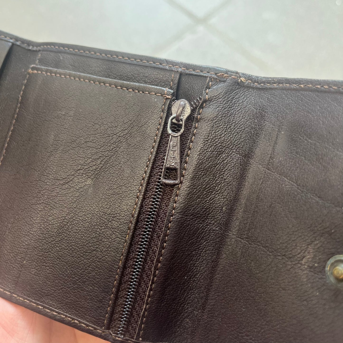 Dolce & Gabbana 2000s Cow-Print Wallet features a brown leather construction with a cow-print pony hair-style panel on the front exterior. A leather patch with a D&G logo is placed over the patterned section. The interior includes multiple compartments, card slots, a top compartment, and a zipped pocket for storage. Made in Italy.
