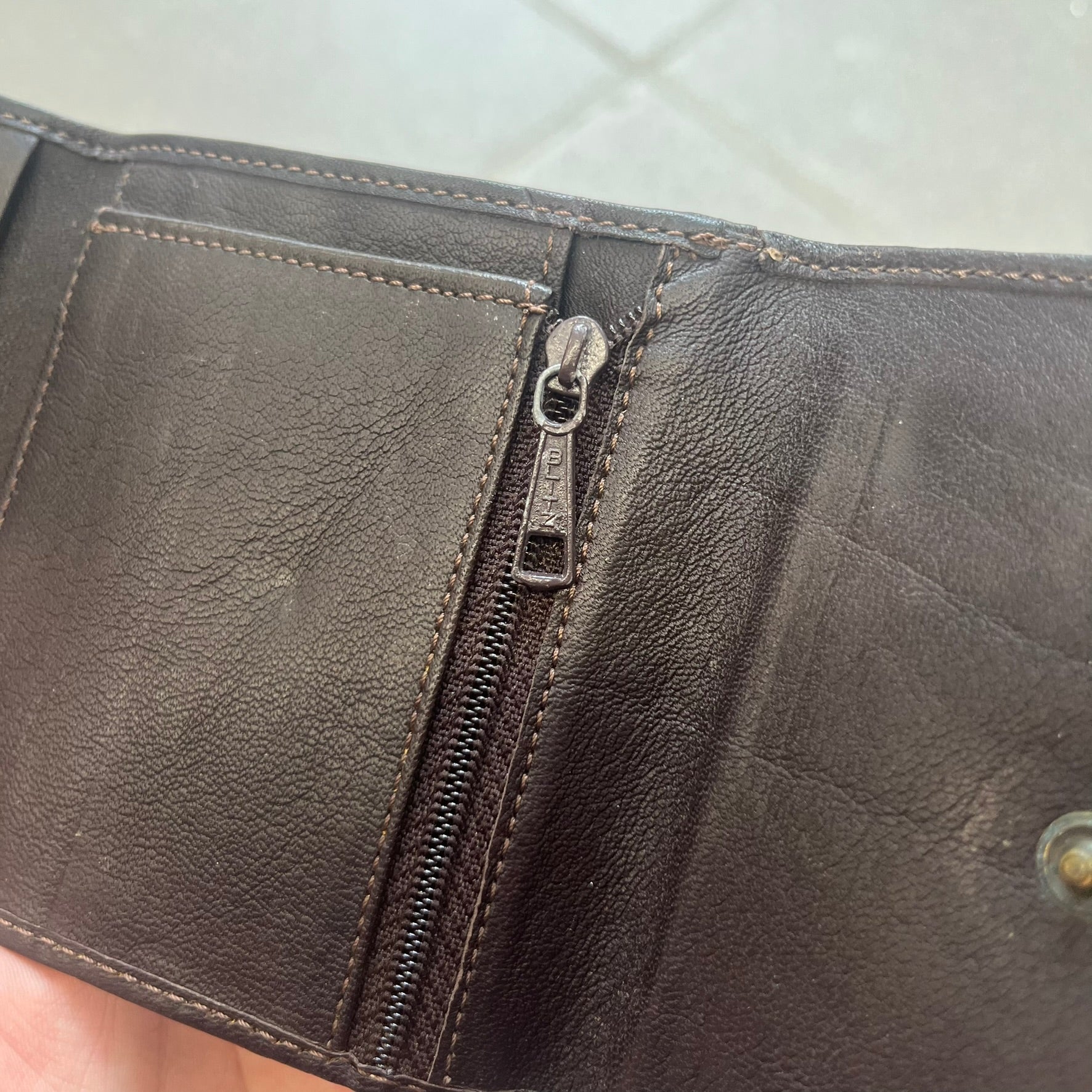 Dolce & Gabbana 2000s Cow-Print Wallet features a brown leather construction with a cow-print pony hair-style panel on the front exterior. A leather patch with a D&G logo is placed over the patterned section. The interior includes multiple compartments, card slots, a top compartment, and a zipped pocket for storage. Made in Italy.
