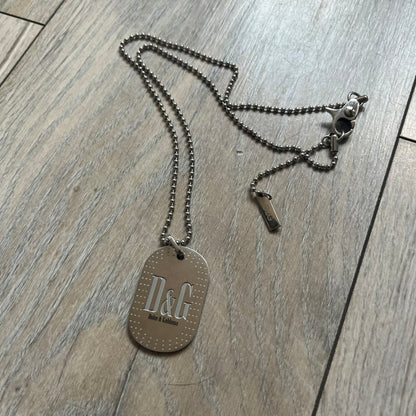 Dolce &amp; Gabbana Cowboy Dog Tag Necklace, model DJ0633. Features a silver-tone metal ball chain and a dog tag with black cowboy-style D&amp;G logo and small “Dolce &amp; Gabbana” text underneath. The front of the tag is patterned with subtle white dots for added detail.