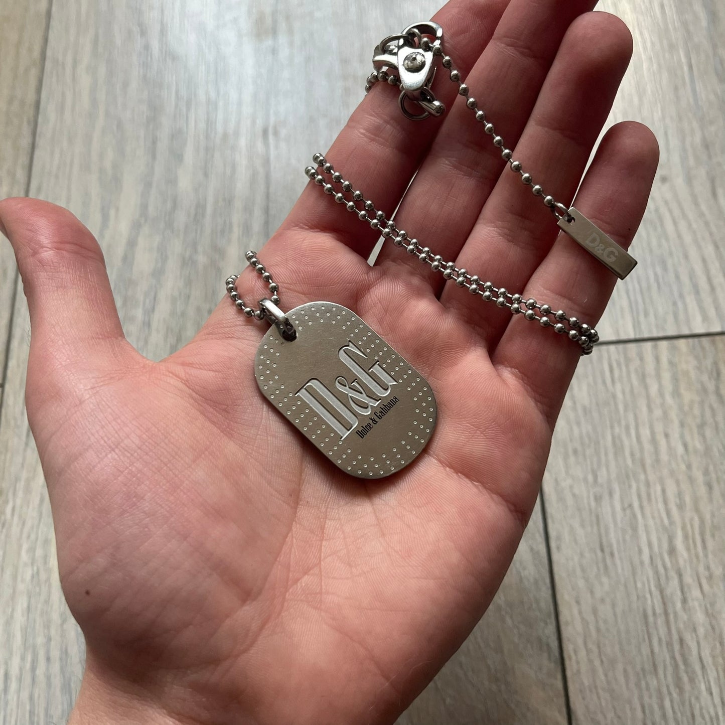 Dolce &amp; Gabbana Cowboy Dog Tag Necklace, model DJ0633. Features a silver-tone metal ball chain and a dog tag with black cowboy-style D&amp;G logo and small “Dolce &amp; Gabbana” text underneath. The front of the tag is patterned with subtle white dots for added detail.