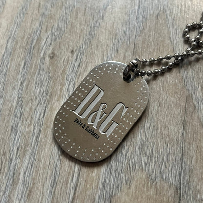 Dolce &amp; Gabbana Cowboy Dog Tag Necklace, model DJ0633. Features a silver-tone metal ball chain and a dog tag with black cowboy-style D&amp;G logo and small “Dolce &amp; Gabbana” text underneath. The front of the tag is patterned with subtle white dots for added detail.