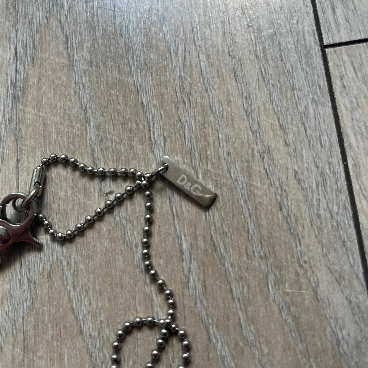 Dolce &amp; Gabbana Cowboy Dog Tag Necklace, model DJ0633. Features a silver-tone metal ball chain and a dog tag with black cowboy-style D&amp;G logo and small “Dolce &amp; Gabbana” text underneath. The front of the tag is patterned with subtle white dots for added detail.