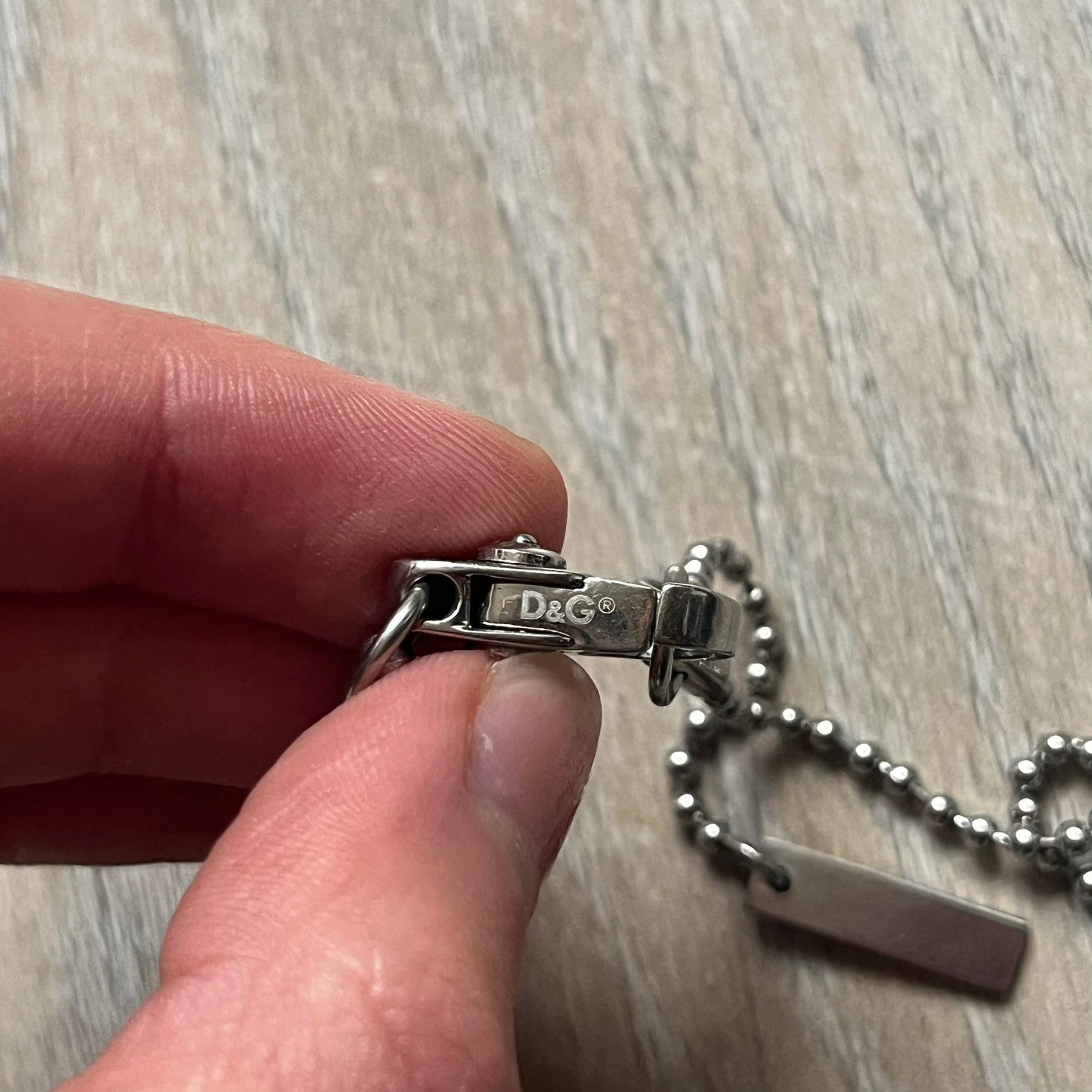 Dolce &amp; Gabbana Cowboy Dog Tag Necklace, model DJ0633. Features a silver-tone metal ball chain and a dog tag with black cowboy-style D&amp;G logo and small “Dolce &amp; Gabbana” text underneath. The front of the tag is patterned with subtle white dots for added detail.