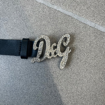 Dolce &amp; Gabbana 2000s Black Crystal Buckle Belt features a black leather strap with a stainless steel D&amp;G logo buckle. The buckle has a decorative italic-style font and is fully covered with crystal/rhinestone detailing on the front. Made in Italy.
