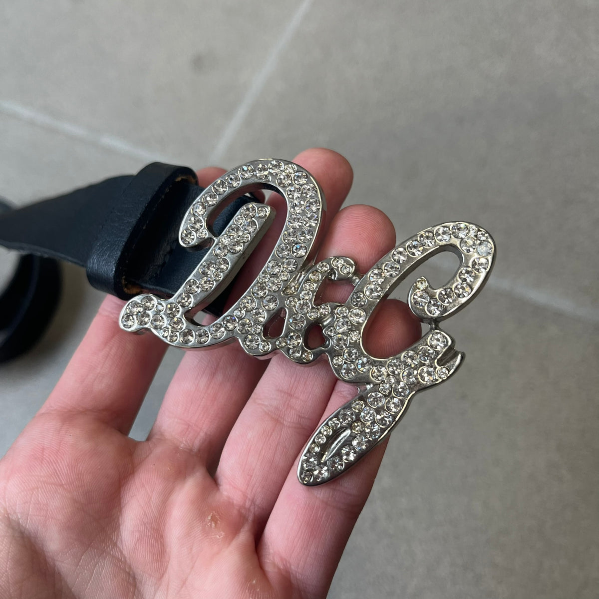 Dolce &amp; Gabbana 2000s Black Crystal Buckle Belt features a black leather strap with a stainless steel D&amp;G logo buckle. The buckle has a decorative italic-style font and is fully covered with crystal/rhinestone detailing on the front. Made in Italy.