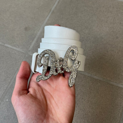 Dolce &amp; Gabbana 2000's Crystal Buckle White Belt features a white leather strap with a stainless steel D&amp;G logo buckle. The buckle has a decorative italic-style font and is fully covered with crystal/rhinestone detailing on the front. Made in Italy.