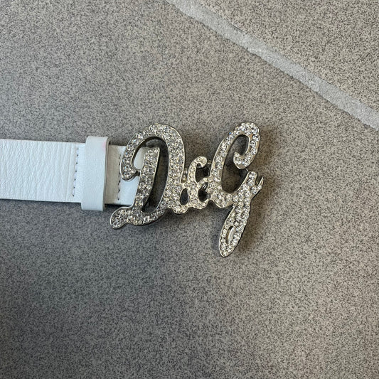 Dolce &amp; Gabbana 2000's Crystal Buckle White Belt features a white leather strap with a stainless steel D&amp;G logo buckle. The buckle has a decorative italic-style font and is fully covered with crystal/rhinestone detailing on the front. Made in Italy.