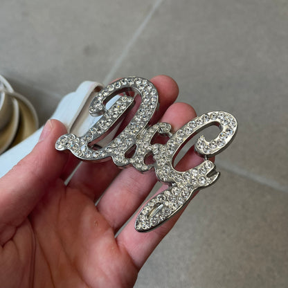 Dolce &amp; Gabbana 2000's Crystal Buckle White Belt features a white leather strap with a stainless steel D&amp;G logo buckle. The buckle has a decorative italic-style font and is fully covered with crystal/rhinestone detailing on the front. Made in Italy.