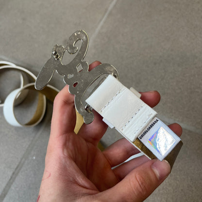 Dolce &amp; Gabbana 2000's Crystal Buckle White Belt features a white leather strap with a stainless steel D&amp;G logo buckle. The buckle has a decorative italic-style font and is fully covered with crystal/rhinestone detailing on the front. Made in Italy.