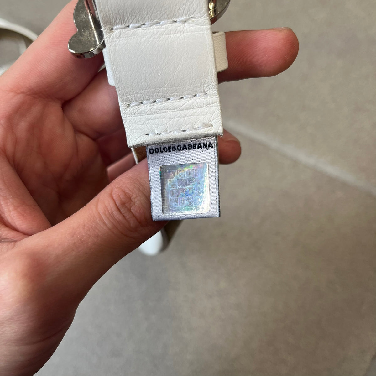 Dolce &amp; Gabbana 2000's Crystal Buckle White Belt features a white leather strap with a stainless steel D&amp;G logo buckle. The buckle has a decorative italic-style font and is fully covered with crystal/rhinestone detailing on the front. Made in Italy.