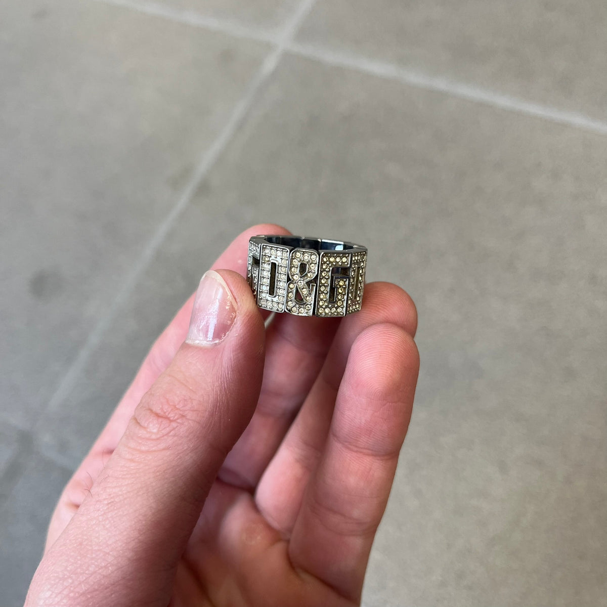 Dolce & Gabbana 2000's Crystal Overlap Ring is a stainless steel ring constructed entirely from cutout D&G letters, forming four repeating D&G sets across 12 letters, each covered in crystals. The ring has slight elasticity, with the letters held together internally by strings.