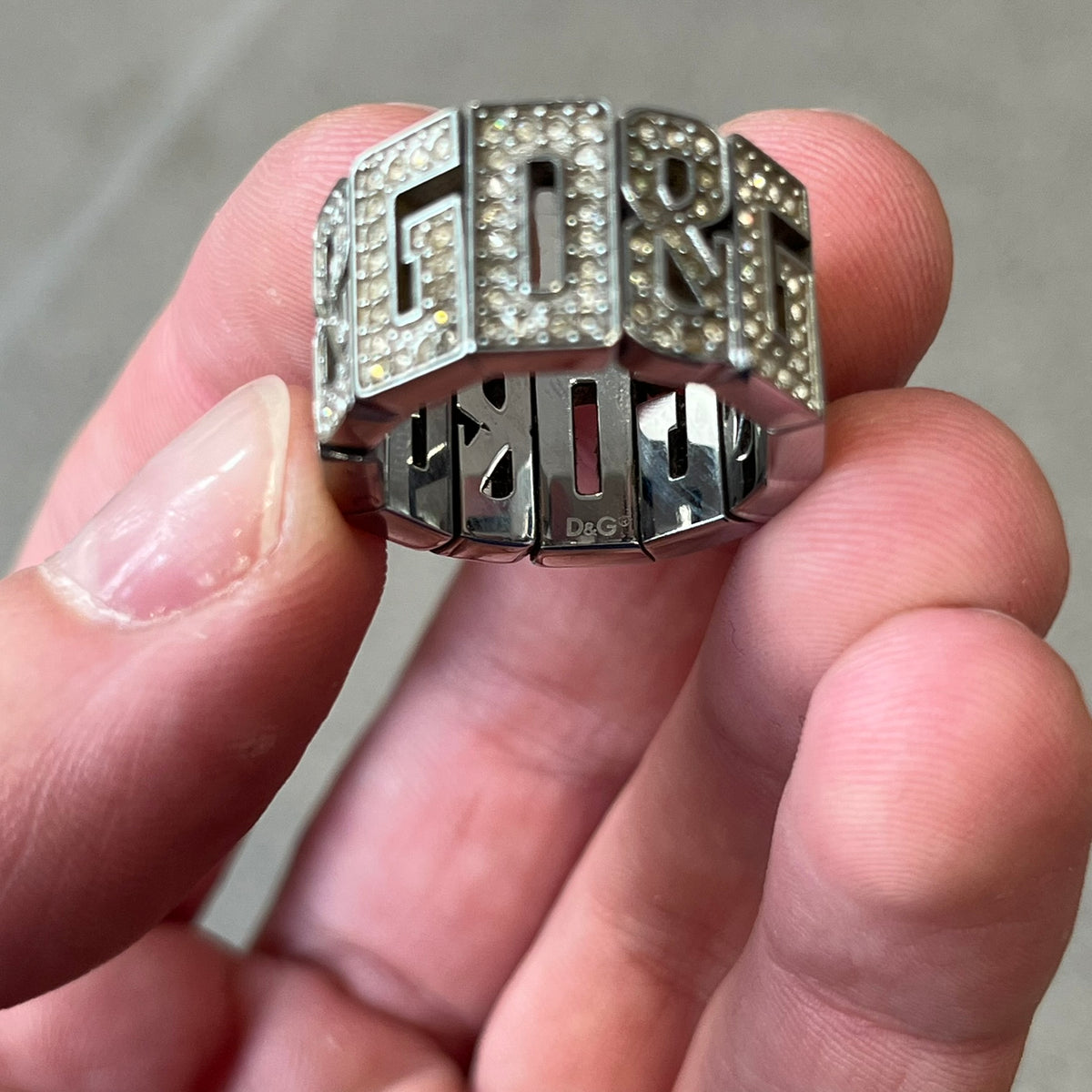 Dolce & Gabbana 2000's Crystal Overlap Ring is a stainless steel ring constructed entirely from cutout D&G letters, forming four repeating D&G sets across 12 letters, each covered in crystals. The ring has slight elasticity, with the letters held together internally by strings.