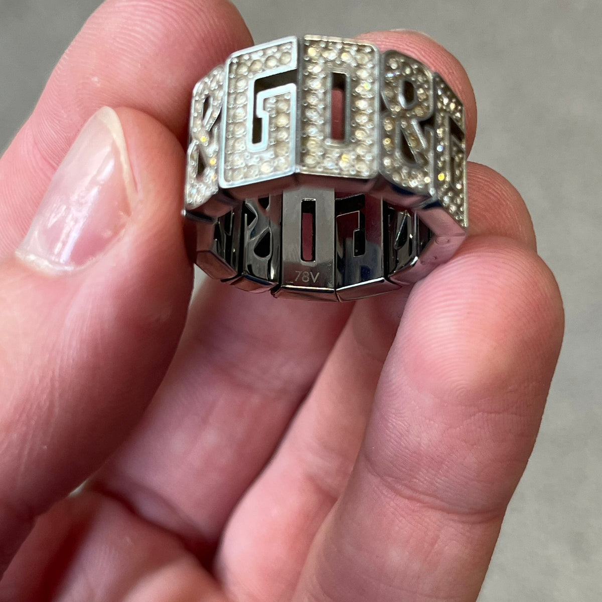 Dolce & Gabbana 2000's Crystal Overlap Ring is a stainless steel ring constructed entirely from cutout D&G letters, forming four repeating D&G sets across 12 letters, each covered in crystals. The ring has slight elasticity, with the letters held together internally by strings.