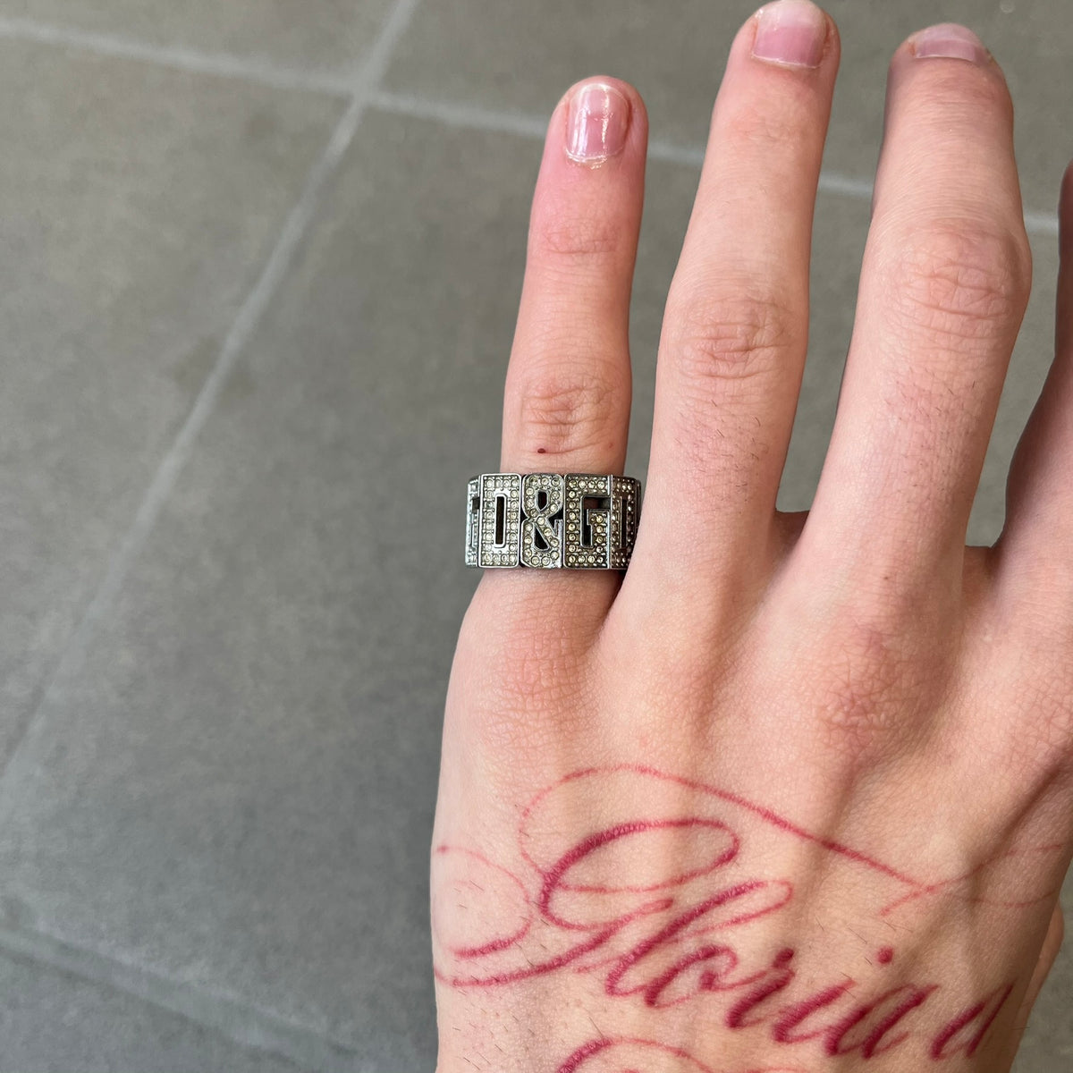 Dolce & Gabbana 2000's Crystal Overlap Ring is a stainless steel ring constructed entirely from cutout D&G letters, forming four repeating D&G sets across 12 letters, each covered in crystals. The ring has slight elasticity, with the letters held together internally by strings.
