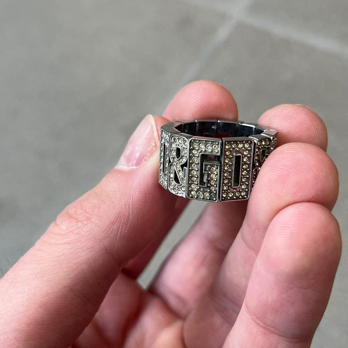 Dolce & Gabbana 2000's Crystal Overlap Ring is a stainless steel ring constructed entirely from cutout D&G letters, forming four repeating D&G sets across 12 letters, each covered in crystals. The ring has slight elasticity, with the letters held together internally by strings.