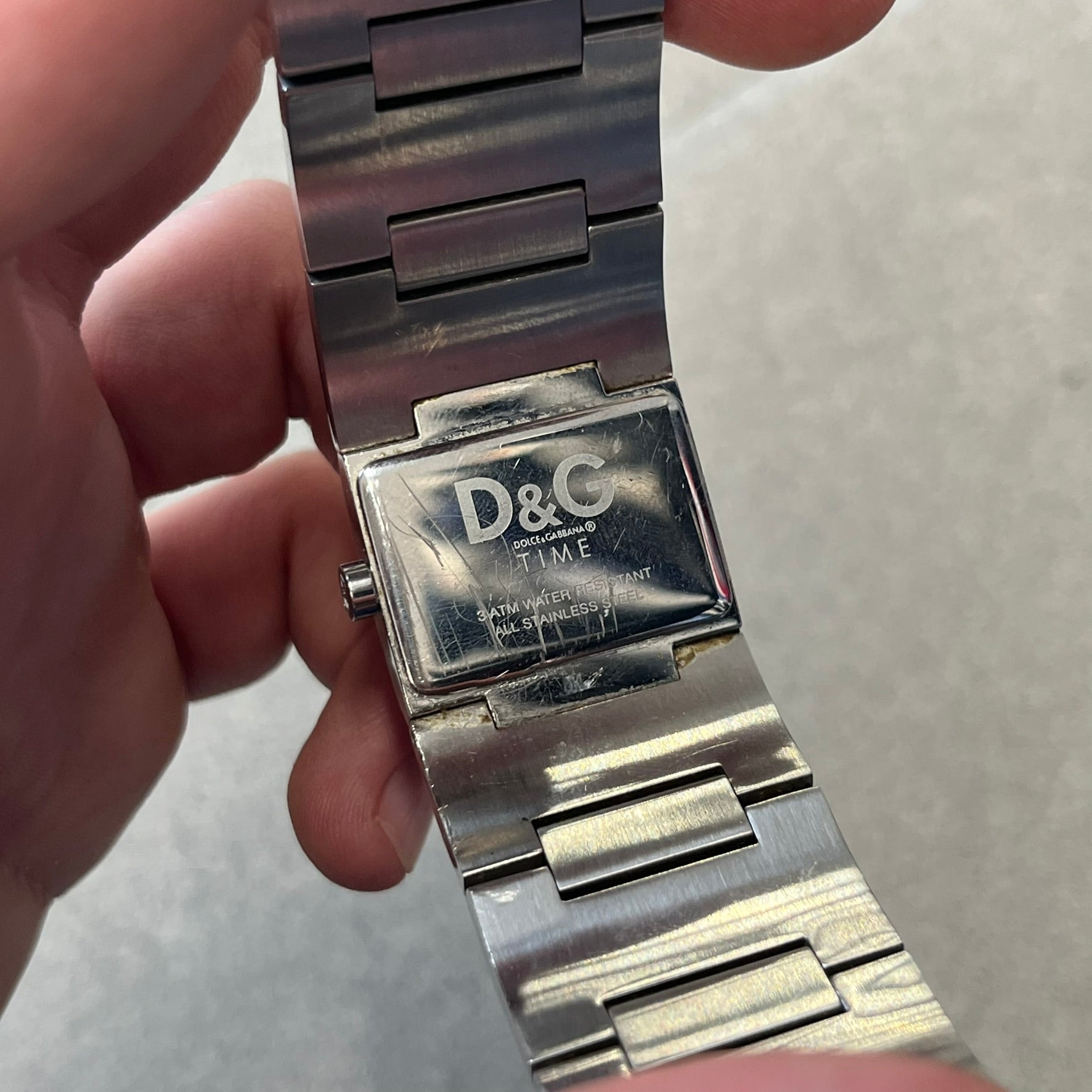 Dolce &amp; Gabbana Crystals Analog Watch is a stainless steel quartz watch featuring a square dial with fully crystal face, silver hands and small D&amp;G logo. The case and bracelet form a continuous design with the face matching the width of the bracelet. The bracelet is made from small silver rectangles. It includes a dual side-clasp closure, is water resistant to 3 ATM, with removable links. Comes with an extra link.