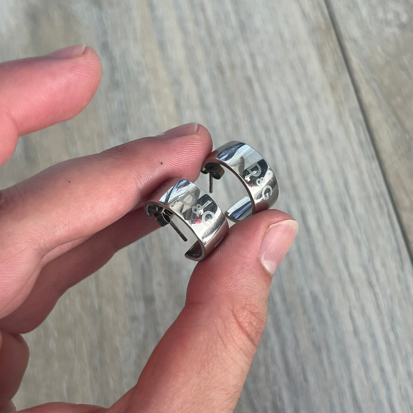 Dolce &amp; Gabbana DJ0404 D&amp;G Logo Earrings are a pair of 2000s silver-tone hoop earrings with a wide profile. The earrings feature an engraved repeating D&amp;G logo around the outer surface. They have a hinged hoop design with a straight post closure and a polished metal finish.