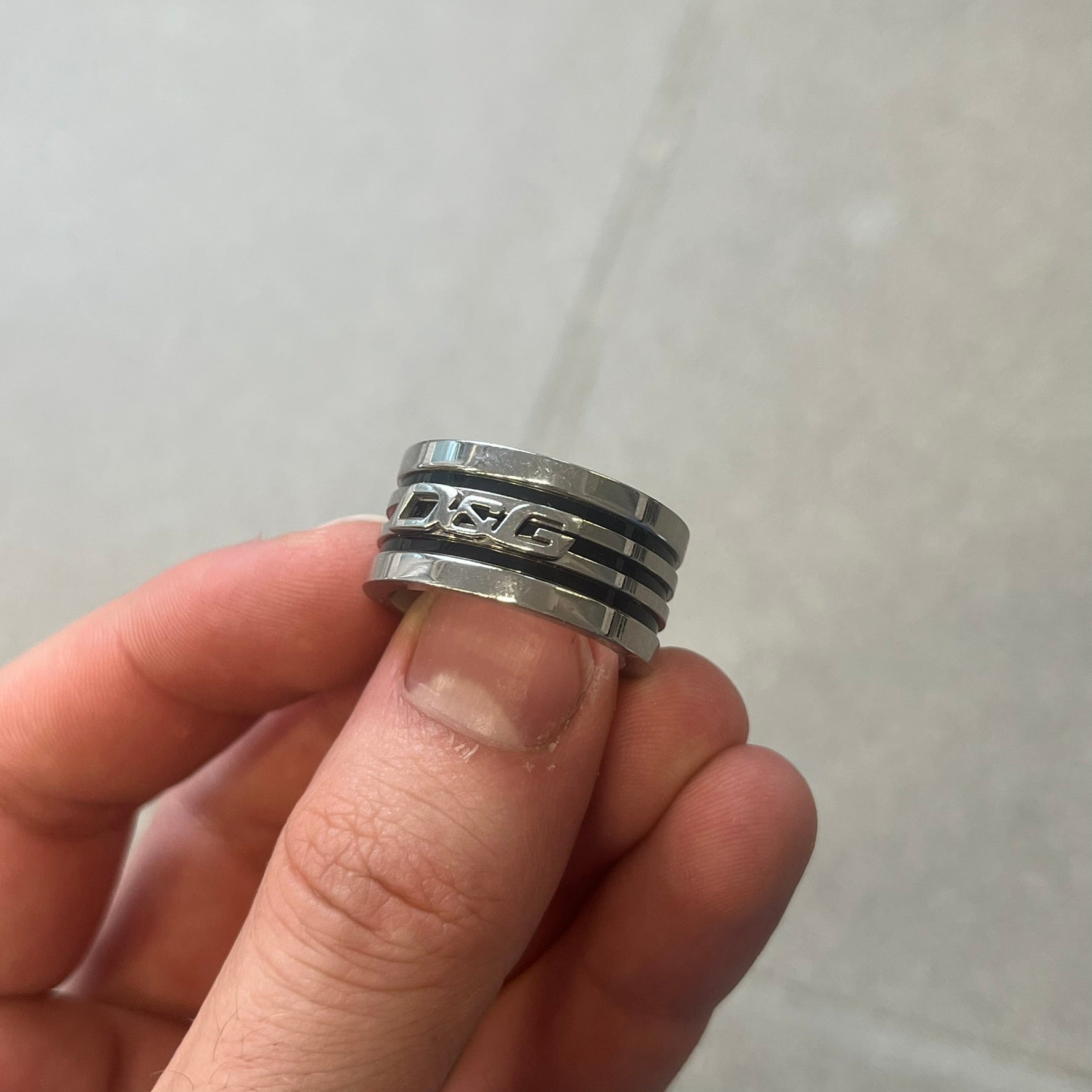 Dolce &amp; Gabbana stainless steel ring DJ0709 in silver, featuring three subtle black engraved stripes encircling the band. The D&amp;G logo is displayed in polished silver on top, creating a nice contrast with the dark detailing.