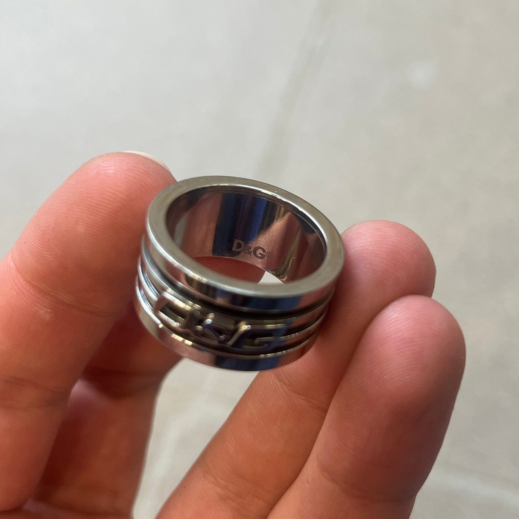 Dolce &amp; Gabbana stainless steel ring DJ0709 in silver, featuring three subtle black engraved stripes encircling the band. The D&amp;G logo is displayed in polished silver on top, creating a nice contrast with the dark detailing.