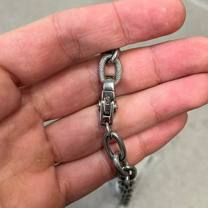 Dolce &amp; Gabbana DJ0879 Four-Leaf Clover Necklace is a stainless steel necklace with a clover pendant that has a stainless steel back and a 3D light beige/cream enamel front. A raised steel D&amp;G logo sits on the front. The oval-link chain alternates between smooth and textured links