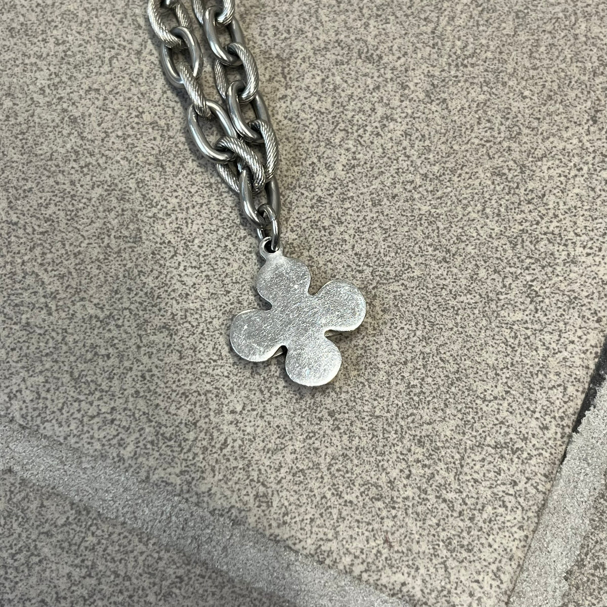 Dolce &amp; Gabbana DJ0879 Four-Leaf Clover Necklace is a stainless steel necklace with a clover pendant that has a stainless steel back and a 3D light beige/cream enamel front. A raised steel D&amp;G logo sits on the front. The oval-link chain alternates between smooth and textured links
