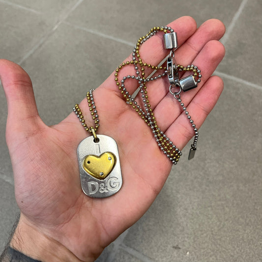 Dolce &amp; Gabbana 2000's Gold Heart DJ0637 Necklace features a stainless steel ball &nbsp;chain, one in silver-tone, the second in gold-tone, with a dog tag-style pendant. The pendant is engraved with a subtle "I" above a gold-tone heart secured by three visible screws, with "D&amp;G" engraved below to form the "I ❤️ D&amp;G" design.&nbsp;