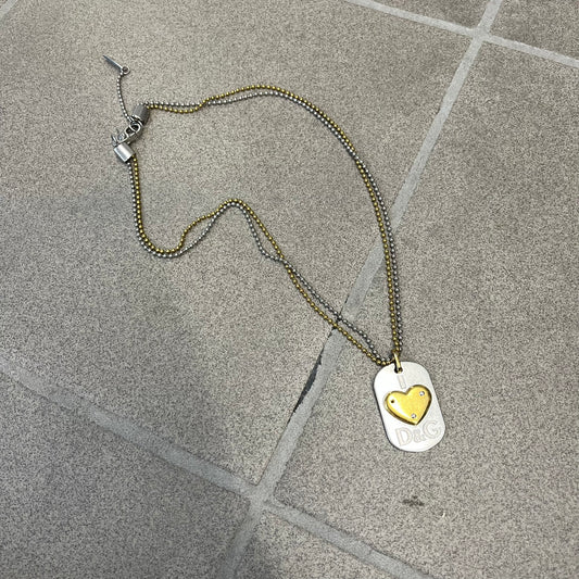 Dolce &amp; Gabbana 2000's Gold Heart DJ0637 Necklace features a stainless steel ball &nbsp;chain, one in silver-tone, the second in gold-tone, with a dog tag-style pendant. The pendant is engraved with a subtle "I" above a gold-tone heart secured by three visible screws, with "D&amp;G" engraved below to form the "I ❤️ D&amp;G" design.&nbsp;