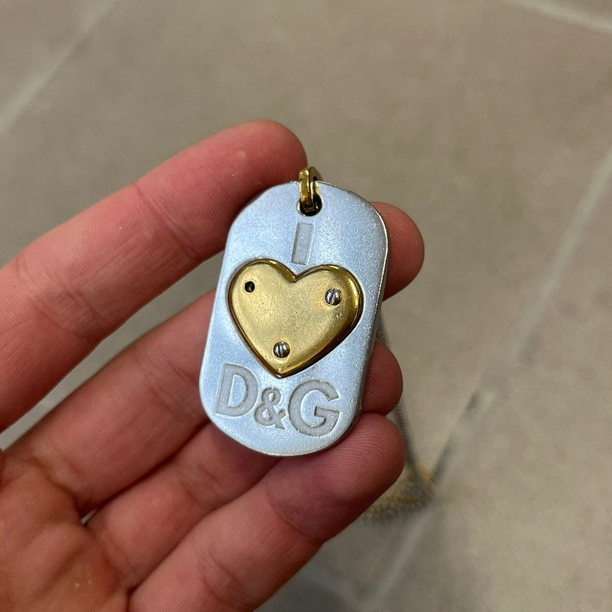 Dolce &amp; Gabbana 2000's Gold Heart DJ0637 Necklace features a stainless steel ball &nbsp;chain, one in silver-tone, the second in gold-tone, with a dog tag-style pendant. The pendant is engraved with a subtle "I" above a gold-tone heart secured by three visible screws, with "D&amp;G" engraved below to form the "I ❤️ D&amp;G" design.&nbsp;