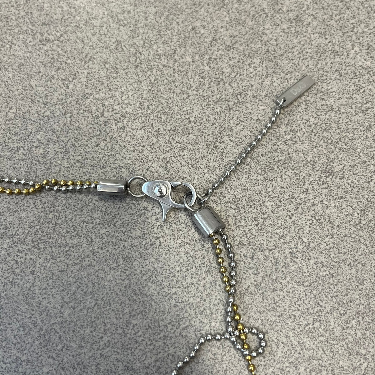 Dolce &amp; Gabbana 2000's Gold Heart DJ0637 Necklace features a stainless steel ball &nbsp;chain, one in silver-tone, the second in gold-tone, with a dog tag-style pendant. The pendant is engraved with a subtle "I" above a gold-tone heart secured by three visible screws, with "D&amp;G" engraved below to form the "I ❤️ D&amp;G" design.&nbsp;