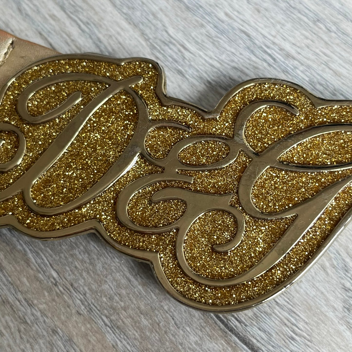 The Dolce &amp; Gabbana 2000’s Gold Tone D&amp;G Logo Belt is made from metallic gold leather and features a large D&amp;G logo buckle shaped directly as the brand’s initials. The buckle uses a cursive D&amp;G logo set over a glittery gold background, framed by a solid gold-tone metal outline. The entire buckle and belt maintain a consistent gold color scheme typical of Dolce &amp; Gabbana accessories from the 2000s.